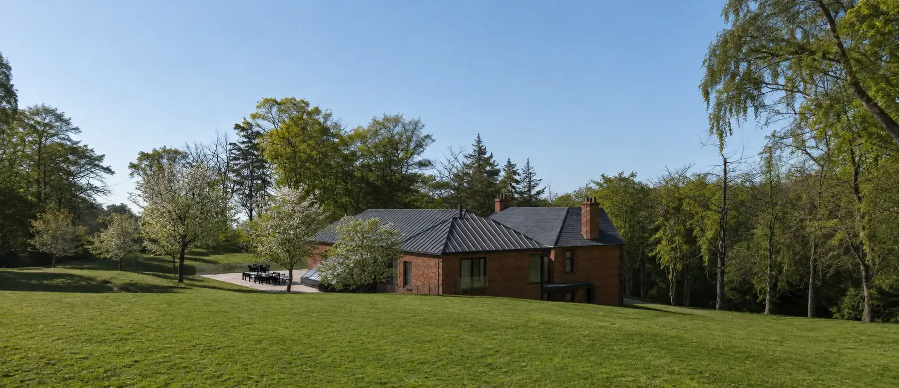 View from the lower lawn: the extension roofs sit low against the trees with the villa chimneys rising behind